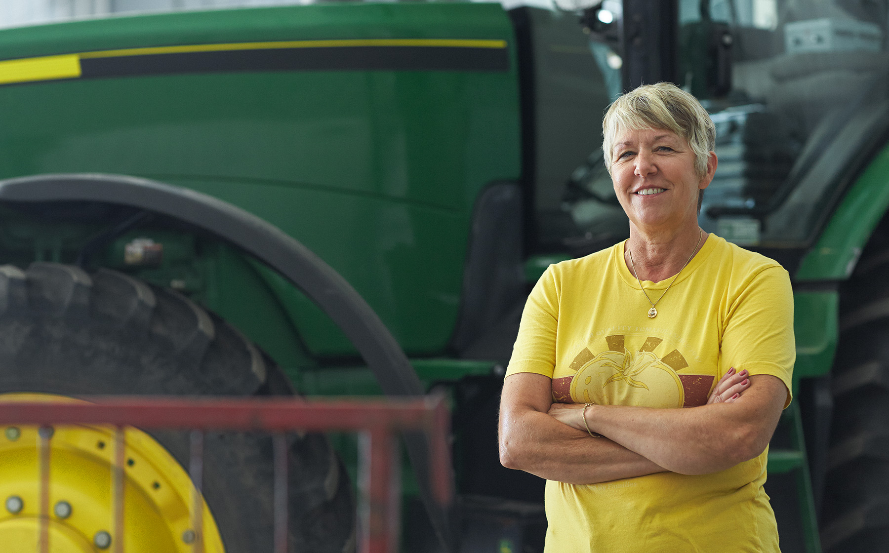 Image of Janice AcMoody wife to Vern who is a Red Gold Tomato grower standing in front of green tractor