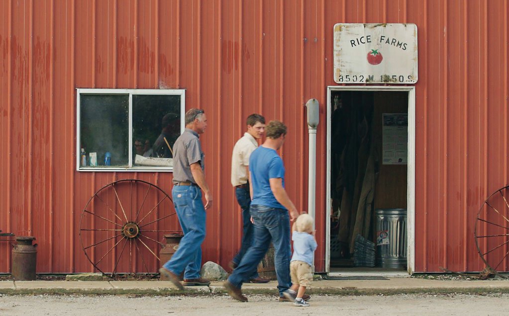 Image of Rice Farms growers for Red Gold tomatoes Scott, James and David and small child head into a red barn
