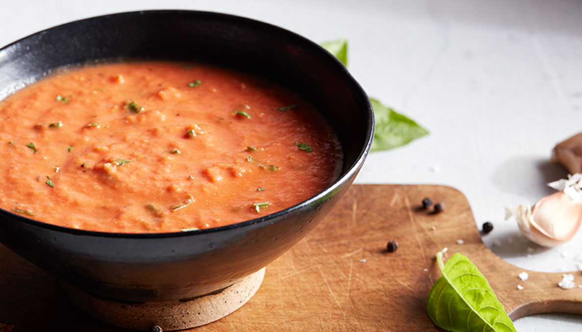 Image of Best Ever Tomato Soup in bowl on cutting board with basil
