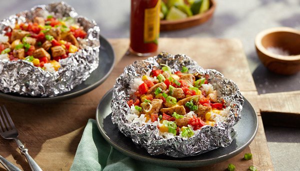 Image of Queso Chicken Foil Packet recipe in tin foil on a wood cutting board from Red Gold Tomatoes