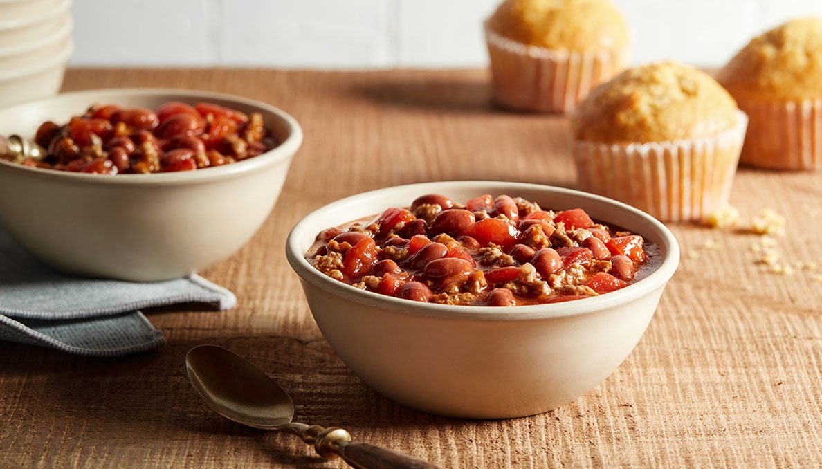 Image of two bowls of Red Gold perfect chili with cornbread muffins in background