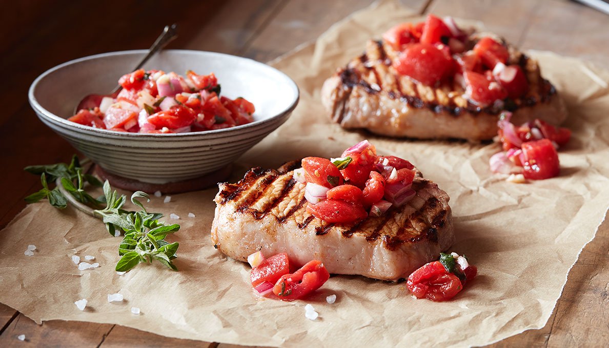 Image of grilled Pork Chops with Tomato Relish on parchment paper and relish in a bowl