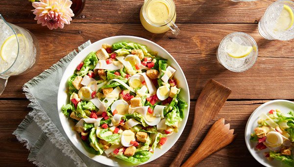 Overhead image of Red Gold Tomatoes Monte Cristo Salad on wood table  with water glasses, plated salad and honey mustard dressing