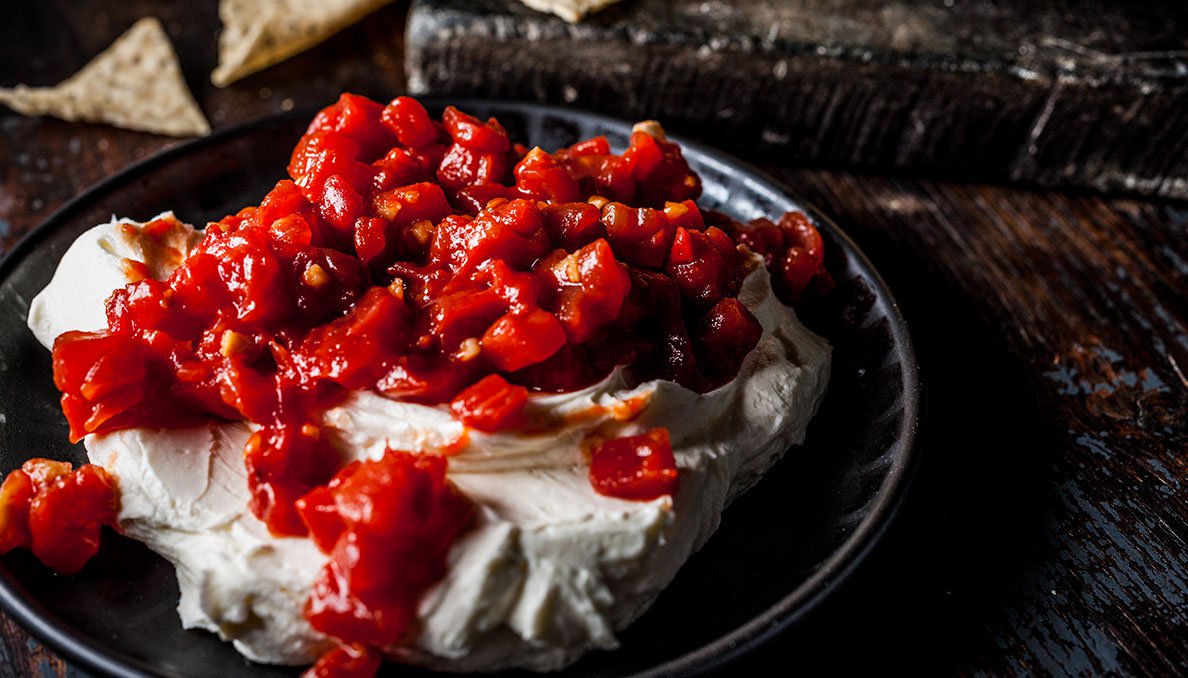 Image of Sriracha Cream Cheese Dip with red gold sriracha petite diced tomatoes over cream cheese on dark plate