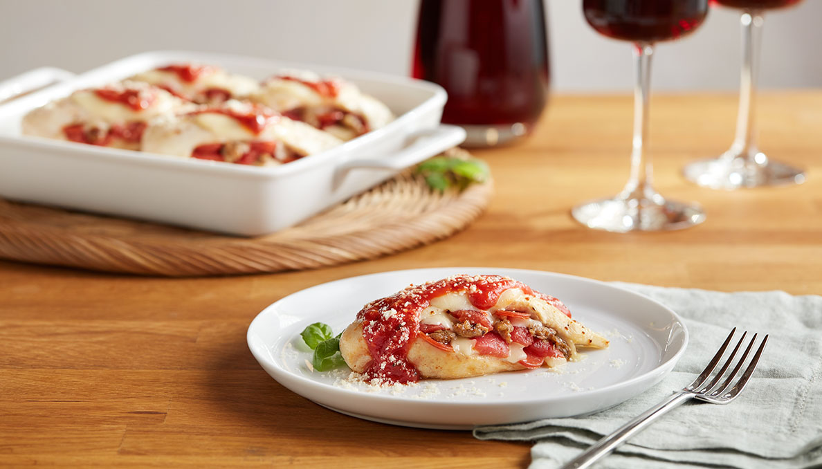 Image of pizza stuffed chicken on white plate and casserole dish in background on wood table