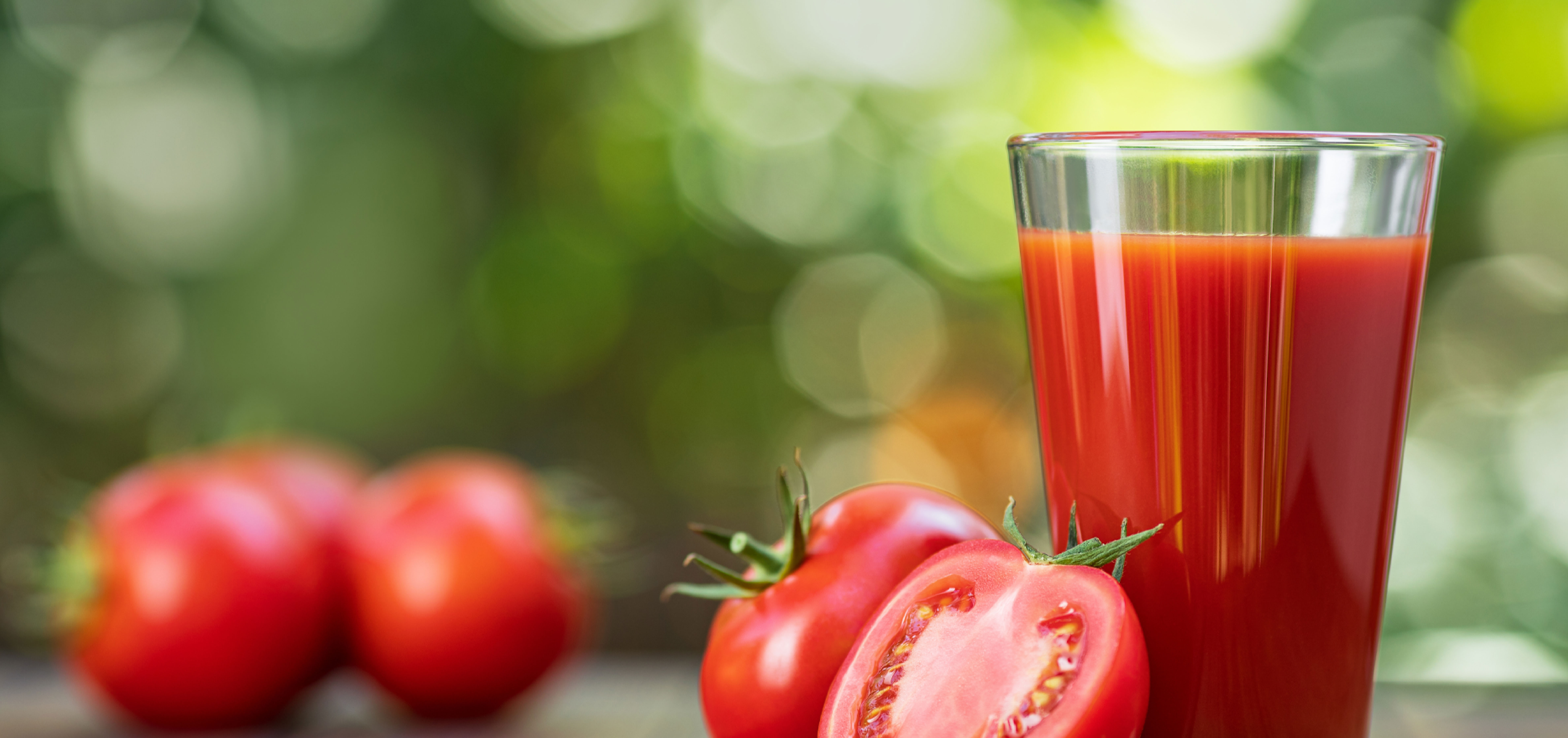 Fresh-squeezed tomato juice in a glass, next to whole, sliced tomatoes.